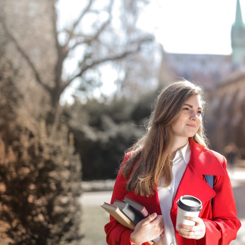 college-student-in-red-coat-holding-notebooks-and-coffee-cup