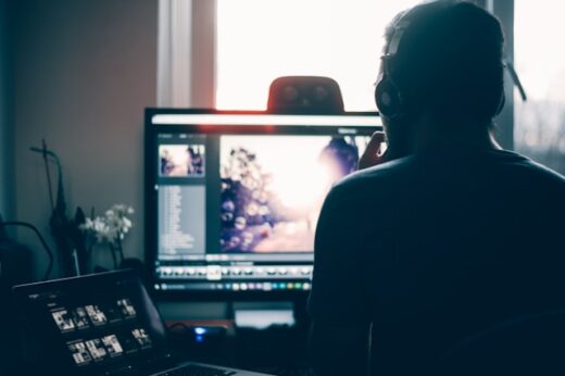 A self-employed professional wearing headphones works on video editing at a dual-screen setup in a home office, symbolizing freelancers managing creative projects and their own health insurance needs.