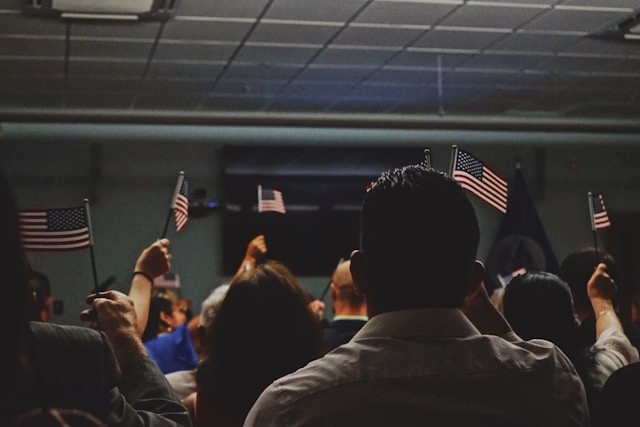 Group of immigrants holding small American flags during a ceremony, symbolizing the search for health insurance for immigrants in the U.S.