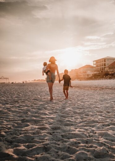 A mother walks along a Florida beach at sunset holding her children’s hands, symbolizing family security and peace of mind with reliable health insurance coverage.